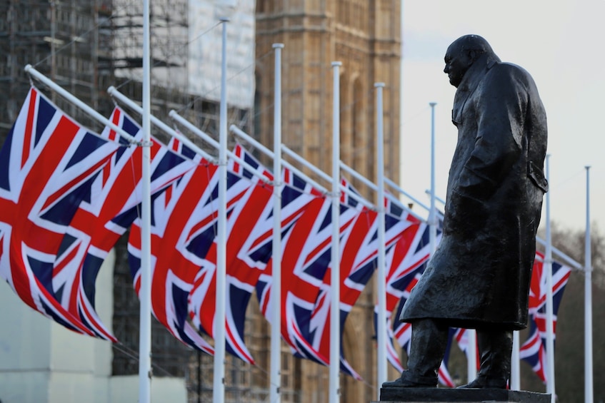 Pitkään takkiin pukeutuneen miehen patsas, jonka ympärillä on useita Union Jack -lippuja. 1