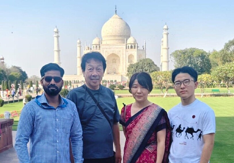 Four people standing in front of the Taj Mahal with its domes and minarets visible in the background. 5