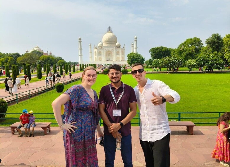 Three people posing in front of the Taj Mahal with a park and visitors in the background. 2