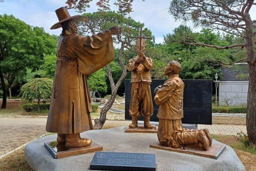 A bronze statue of a man in a hat, a kneeling figure, and another holding a staff in a park. 4