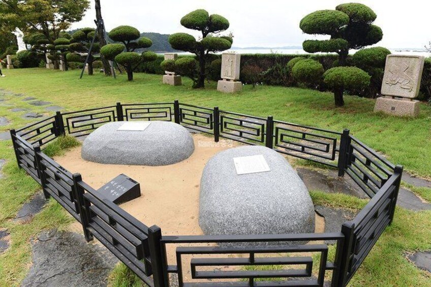 A Zen garden with two large rocks, a wooden fence, and neatly trimmed bushes. 2