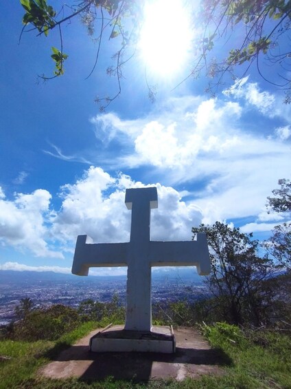 A large white cross on a hilltop with a cityscape in the background. 1
