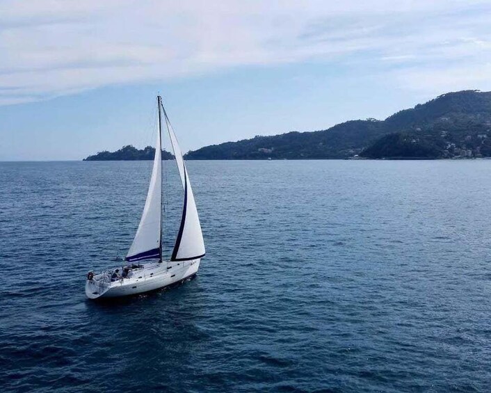 A sailboat on calm waters with a hilly coastline in the background. 1