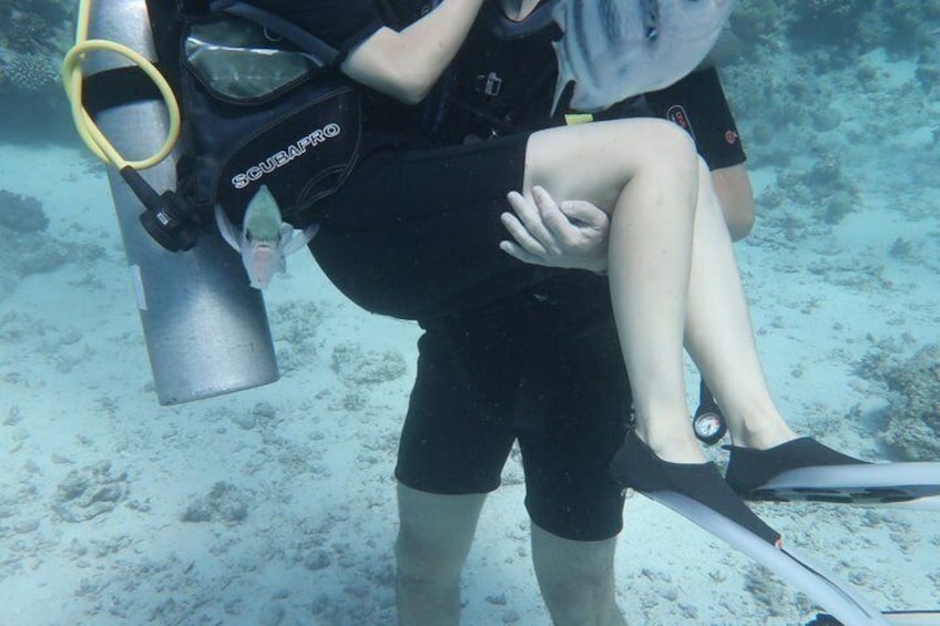 A diver with a SCUBA PRO tank and fins, sitting on another diver's lap underwater. 5