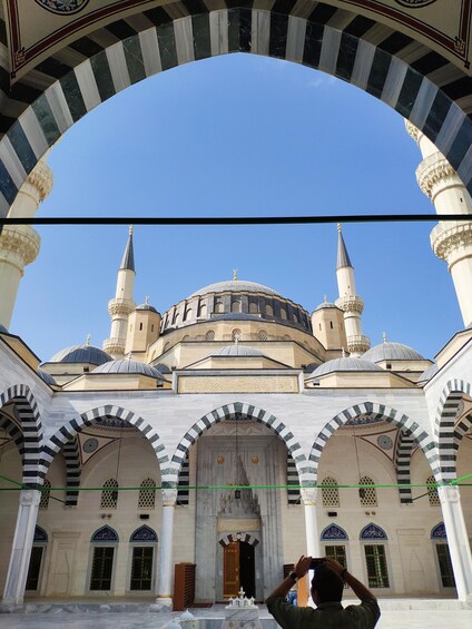 A mosque with a large central dome and two minarets, under a striped archway. 2