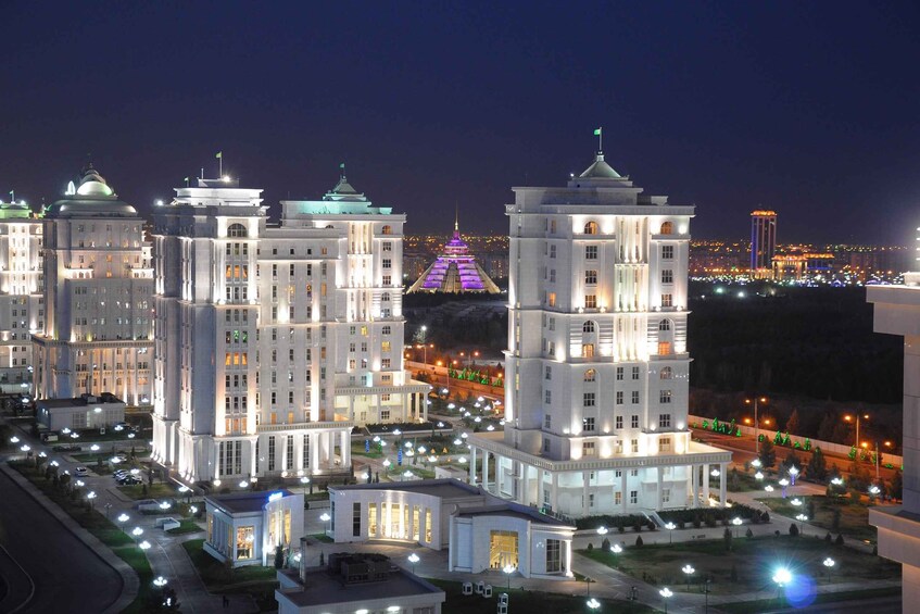 A cityscape at night with illuminated buildings and a distant pyramid-like structure. 1