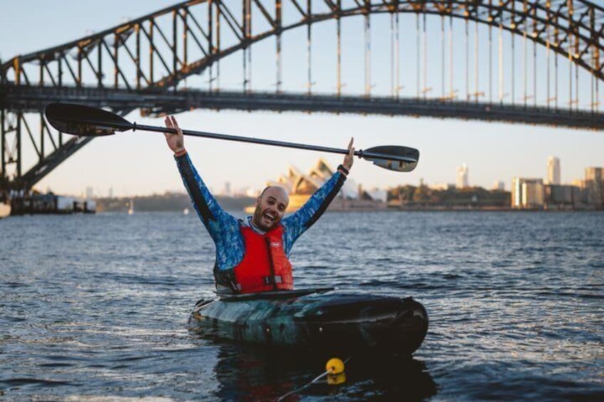 A person kayaking with a paddle, wearing a life jacket, and a city bridge in the background. 2