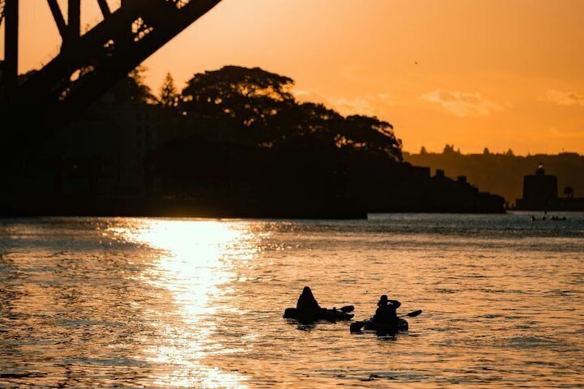 A sunset over a body of water with a bridge and trees in the background. 1