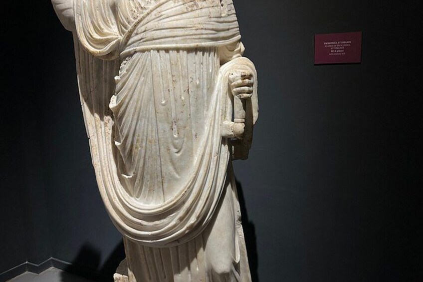 Una estatua de mármol con vestimenta drapeada y un brazo levantado, expuesta en un museo. 3