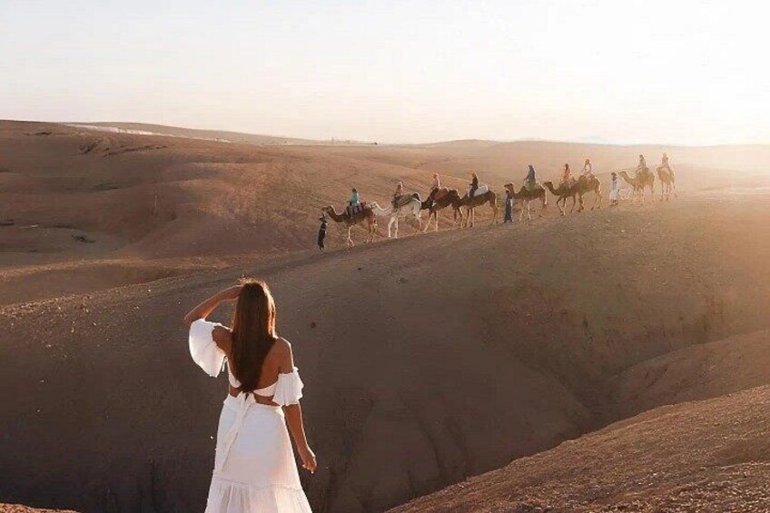 A desert landscape with a group of people riding camels. 5