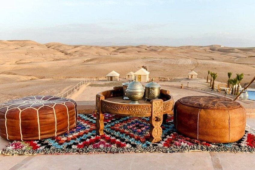 A desert landscape with traditional tents and a colorful rug with ottomans. 2