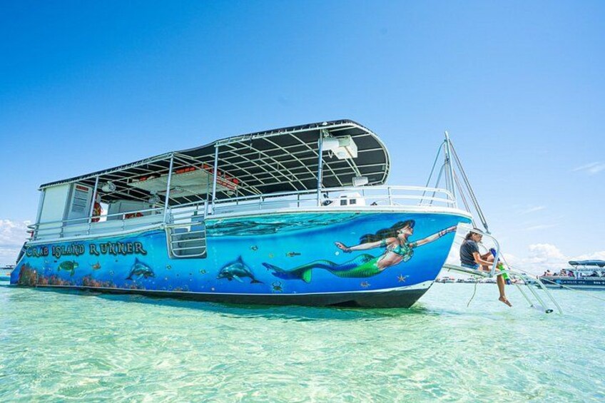 Un bote con un mural de sirena, agua turquesa cristalina y una persona de pie en la popa. 4