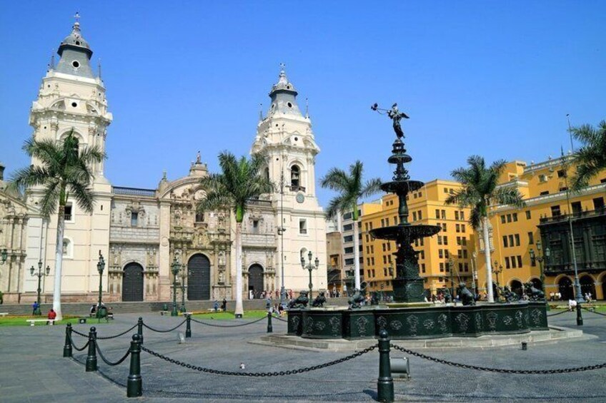 A historic plaza with colonial architecture, a fountain, and palm trees. 1