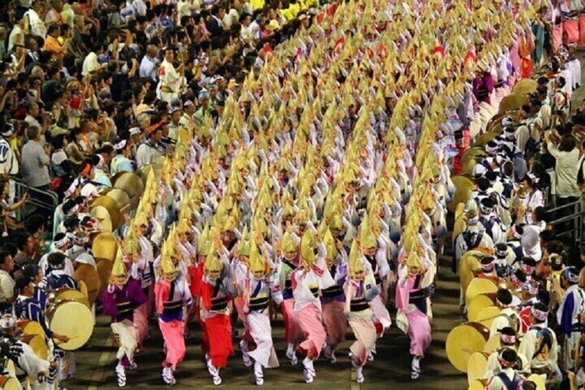 A large group of people in colorful costumes performing a synchronized dance in a crowded venue. 2