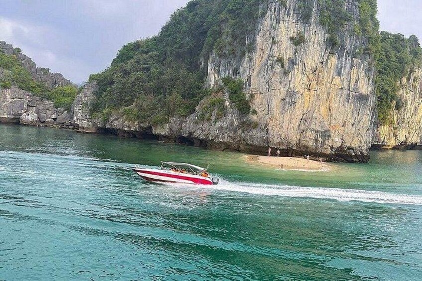 A boat speeding across turquoise water, a rocky cliff, and a beach with people. 2