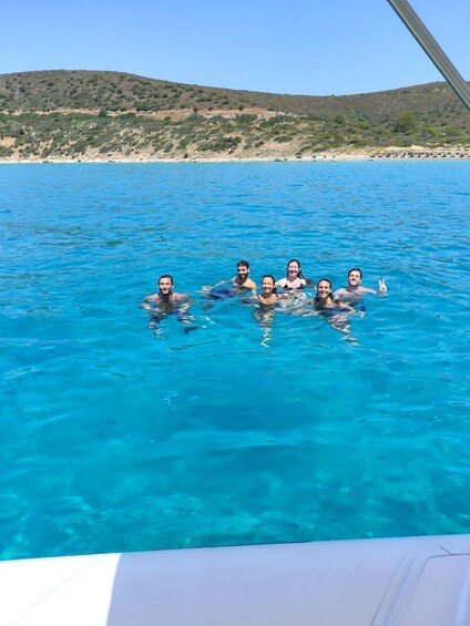 A group of people swimming in a clear blue sea with a hilly landscape in the background. 2