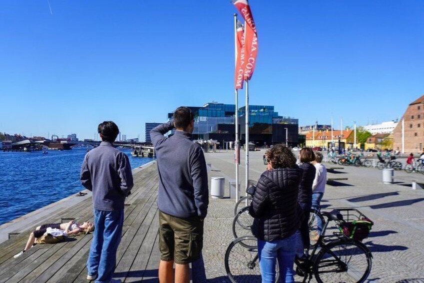 A wooden boardwalk by a body of water with people, bicycles, and a flag. 2