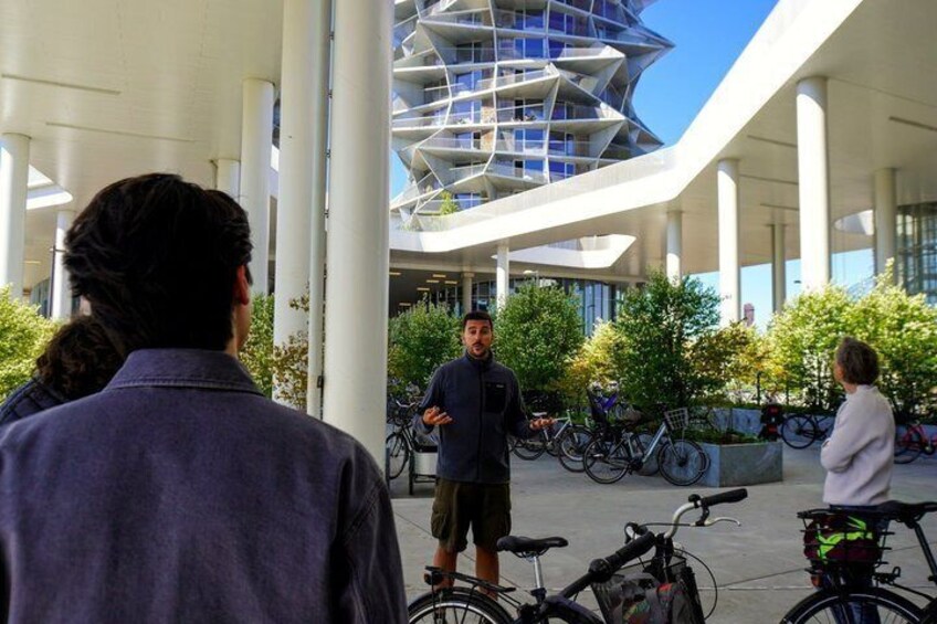 A modern building with a unique geometric design, people standing and talking, and bicycles parked nearby. 5