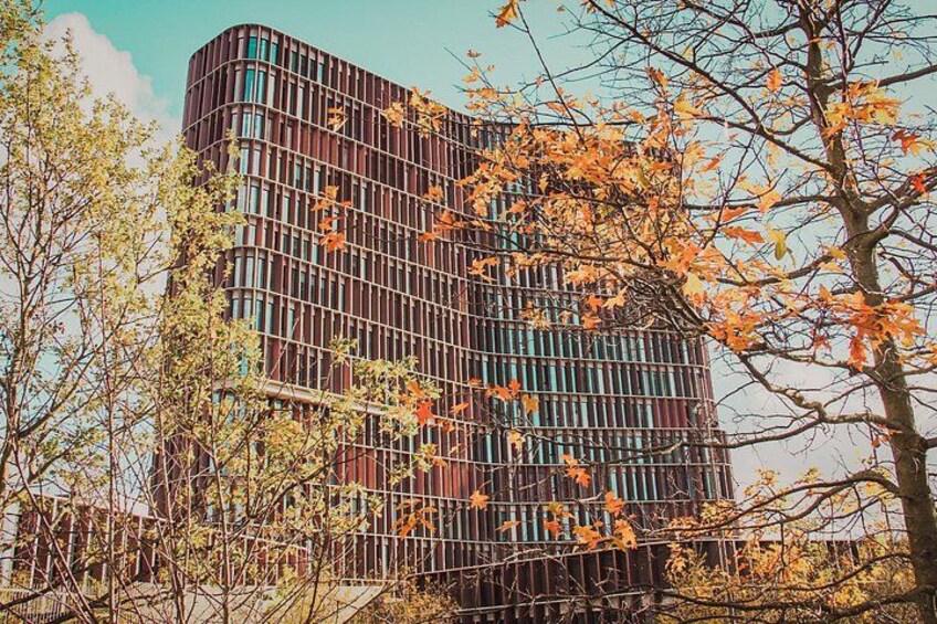 A modern building with a curved facade, surrounded by trees with autumn leaves. 3