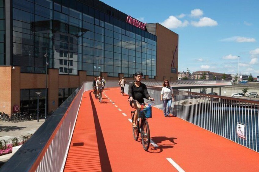 A red bike path with cyclists, a modern building with glass facade, and a clear sky. 3