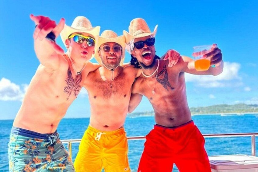 Three people on a boat, wearing hats and sunglasses, with a clear blue sky and ocean in the background. 4