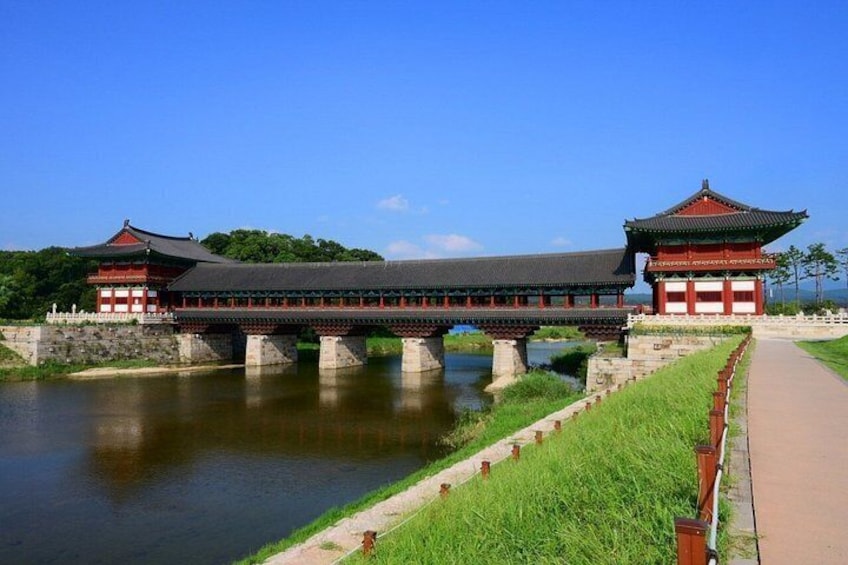 A traditional Korean bridge over a calm river, with a pathway on the right and lush greenery in the background. 2