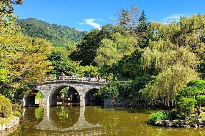 A stone bridge over a pond surrounded by lush greenery and trees. 3