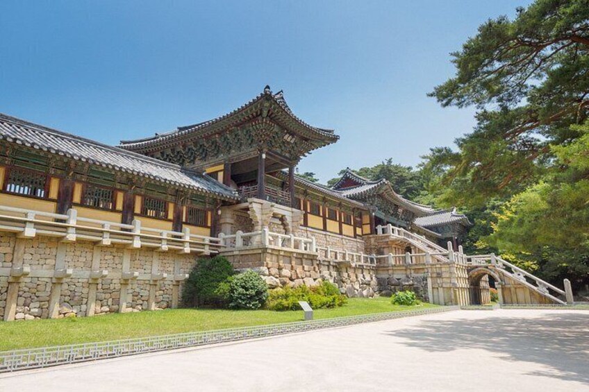 A traditional Korean palace with ornate architecture, a stone wall, and a well-maintained garden. 4