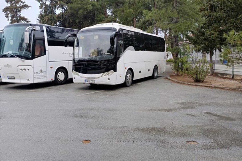 Two white tour buses parked in a lot with trees and a building in the background. 3