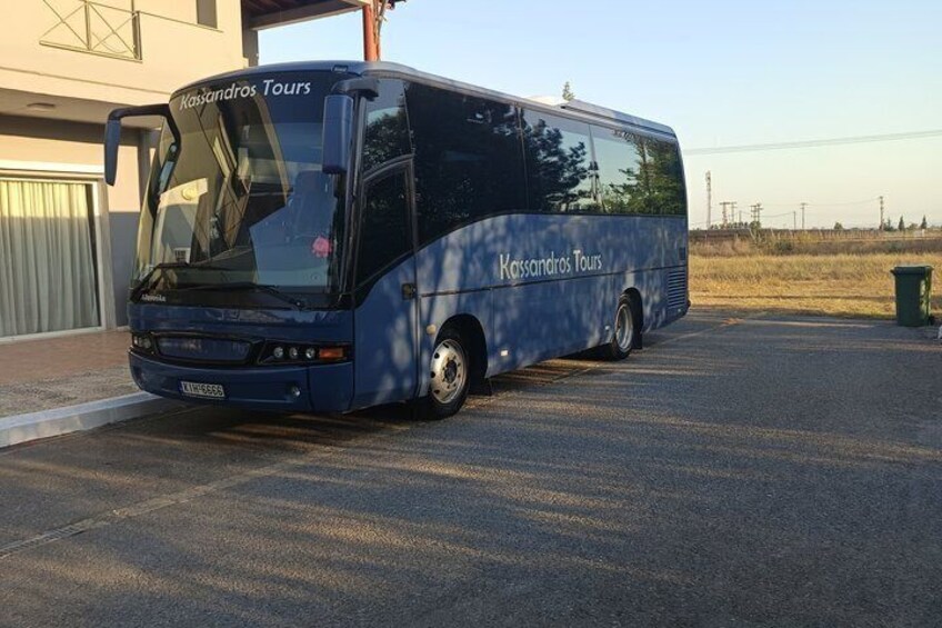 A blue tour bus parked in a lot with a building in the background. 5