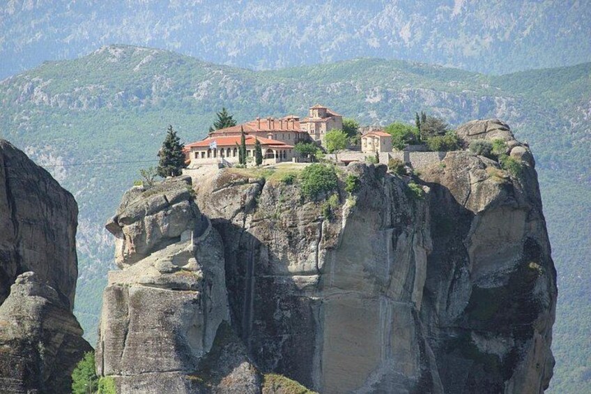 A monastery on a rocky cliff with a mountainous backdrop. 3