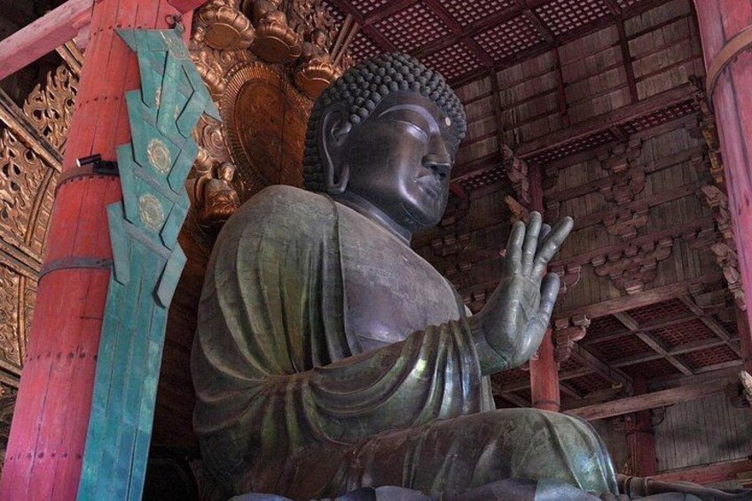 A large bronze Buddha statue in a temple with intricate wooden architecture. 4