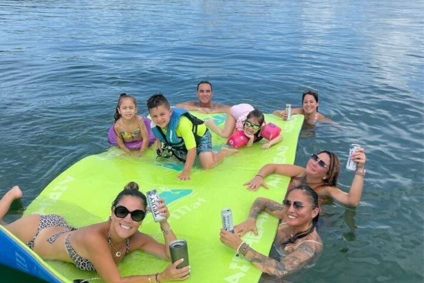 A group of people on a green floating platform in a body of water. 1
