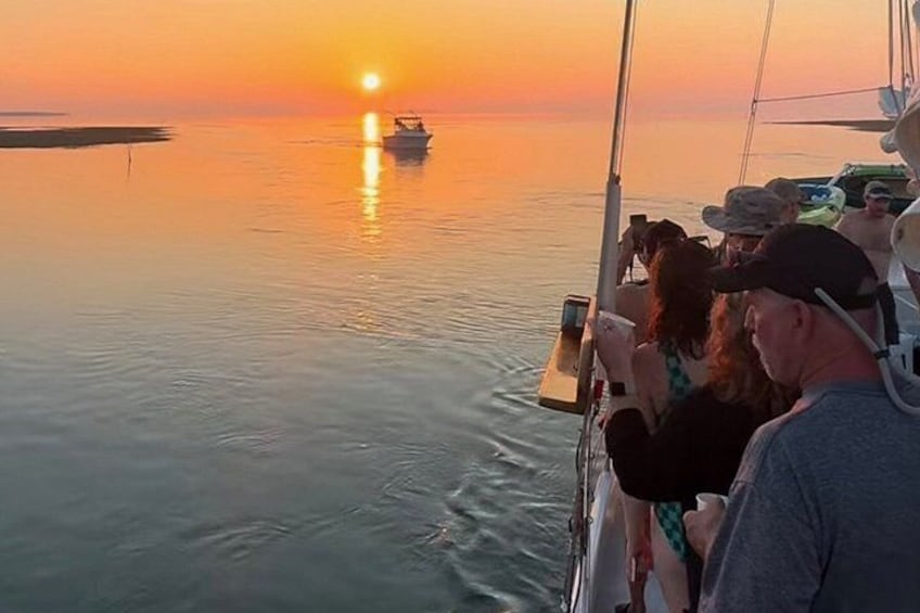 A sunset over calm waters with a boat and people on a dock. 3
