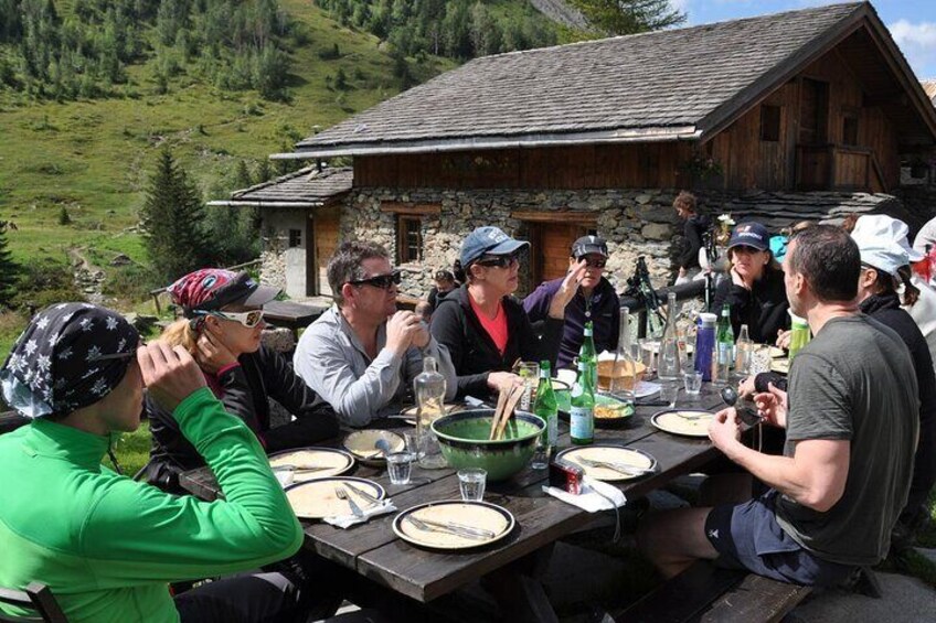 A group of people dining outdoors at a wooden table with a mountainous backdrop. 2