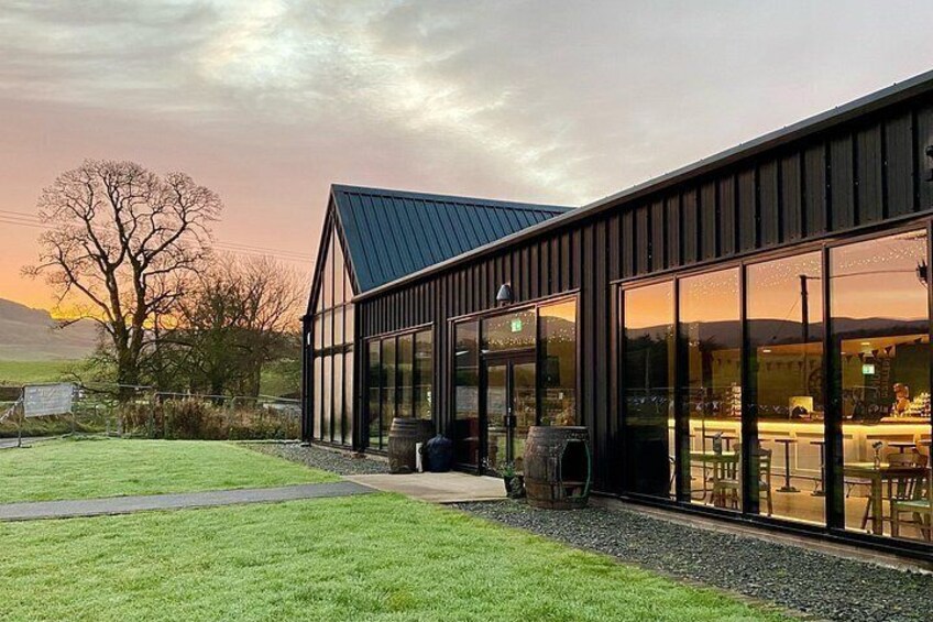 A modern building with large windows and a metal roof, surrounded by a grassy area and a gravel path. 3
