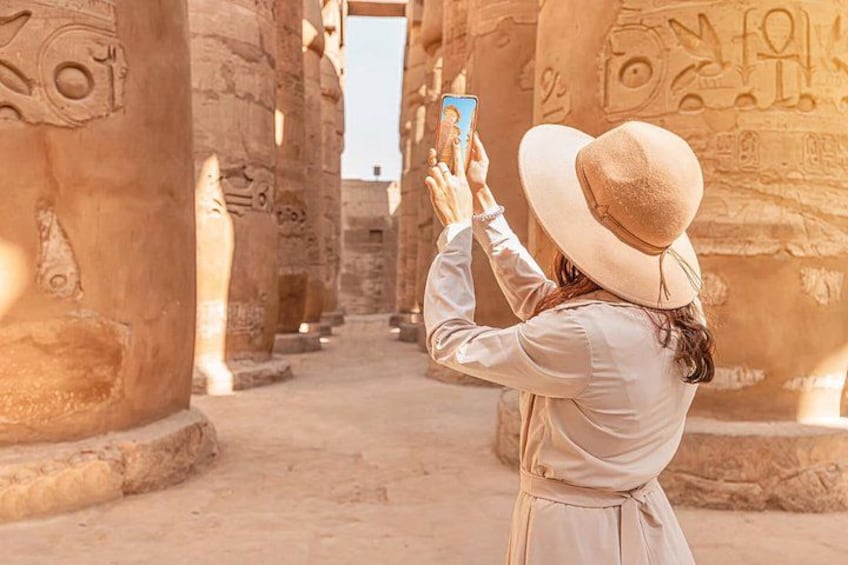 Una persona tomando una foto con un teléfono inteligente en un templo egipcio antiguo, con altas columnas de piedra y jeroglíficos. 2