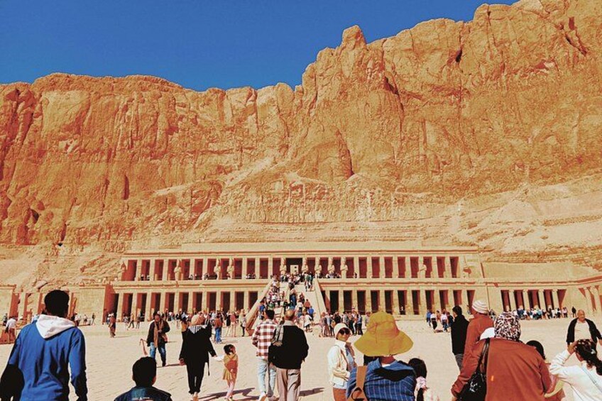 Un grande tempio egizio antico con una lunga colonnata e una folla di turisti di fronte. 5