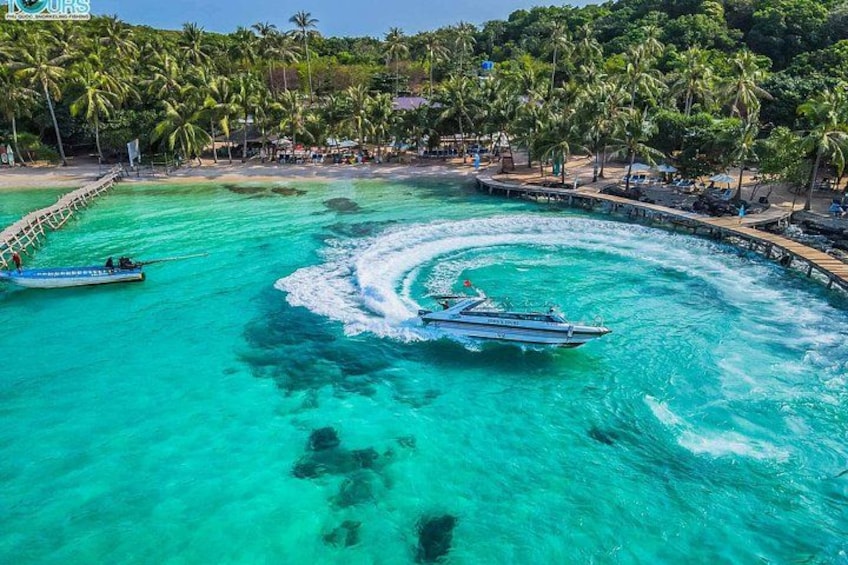 Un bote dejando estela en aguas turquesas, rodeado por una playa con palmeras y un muelle. 5