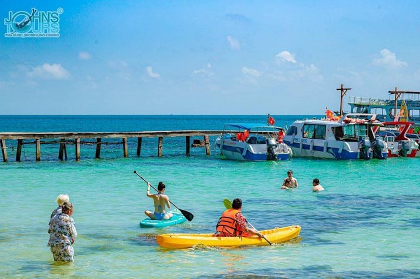 Personas haciendo kayak, un muelle y barcos en un mar azul y transparente. 3