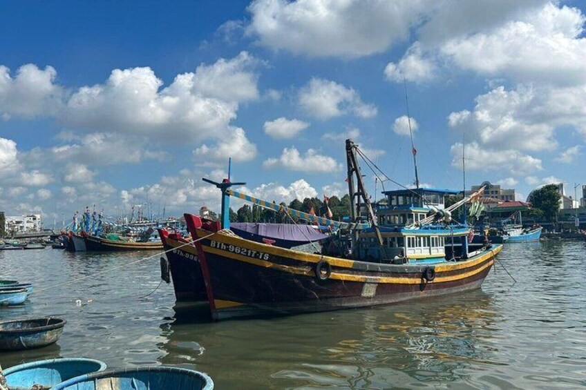 A harbor with several fishing boats docked, a clear sky, and buildings in the background. 5