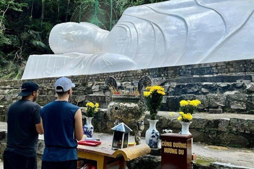 A large white statue of a reclining figure, a stone wall, and a table with vases and flowers. 3