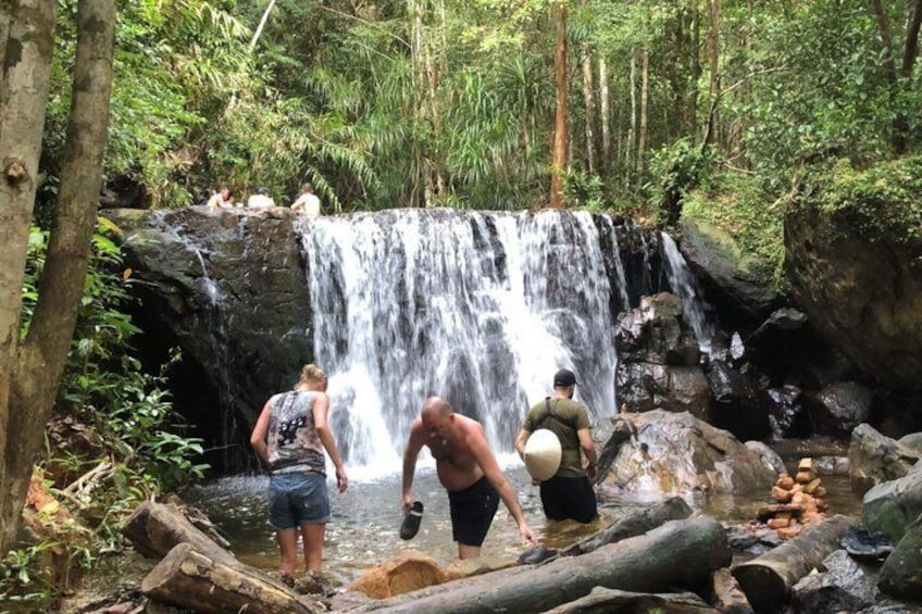 A waterfall in a forested area with people standing and interacting near the water. 4