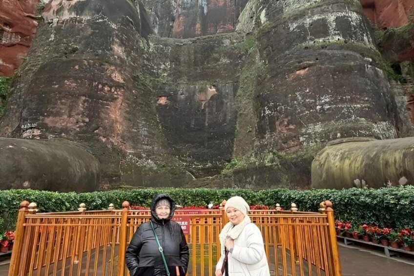 Two people standing in front of a rock formation with a wooden fence and potted plants. 5