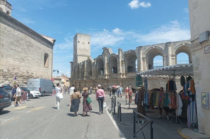 A street with pedestrians, a market stall, and historical arches in the background. 4