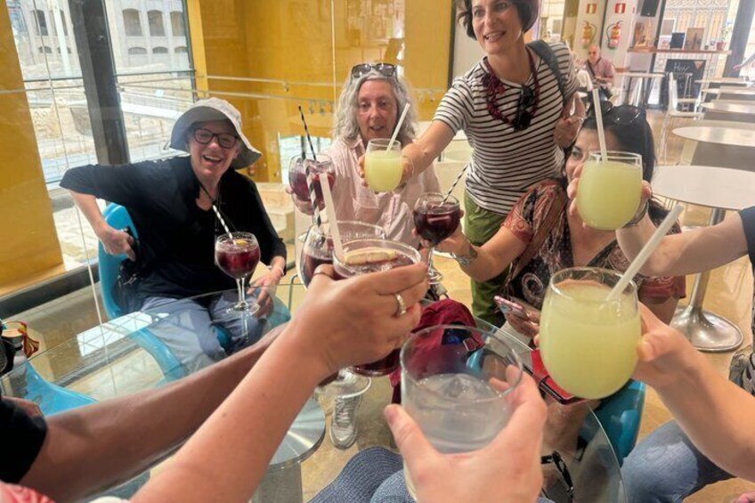 A group of people toasting with drinks at a table in a cafe with large windows. 5