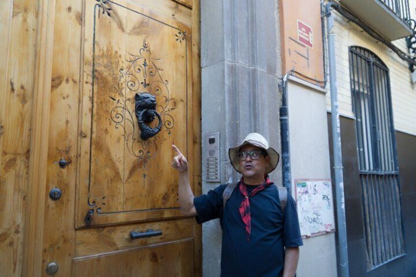 A person pointing at a wooden door with a decorative knocker. 5