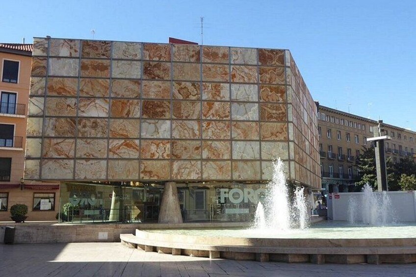 A modern building with a tiled facade, a fountain, and a clear sky. 2