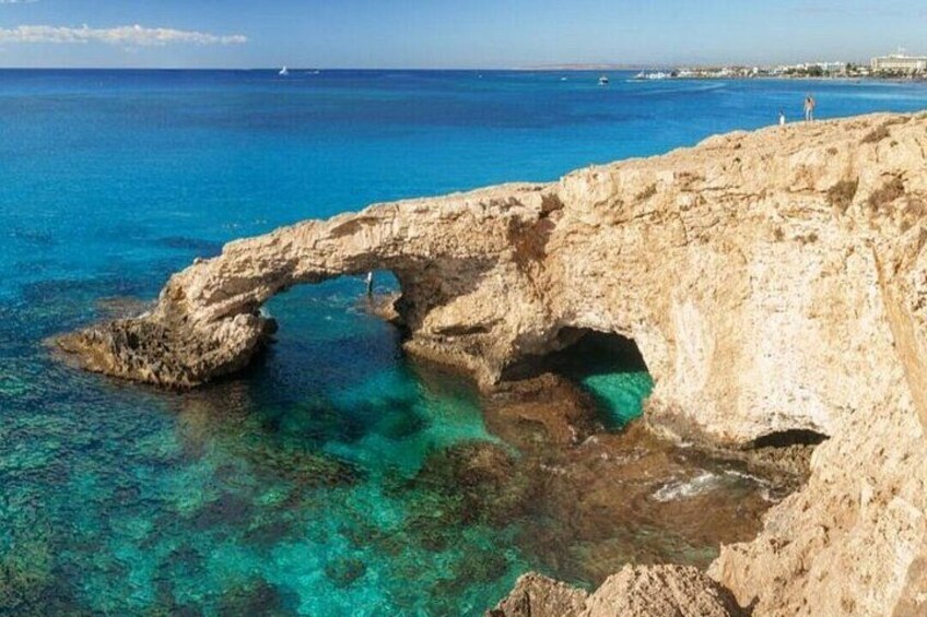 A natural rock arch formation in clear blue waters, surrounded by rocky terrain. 3