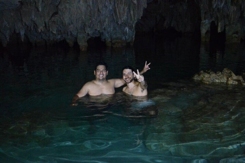 Two people in a cave pool with clear water and rocky formations. 5